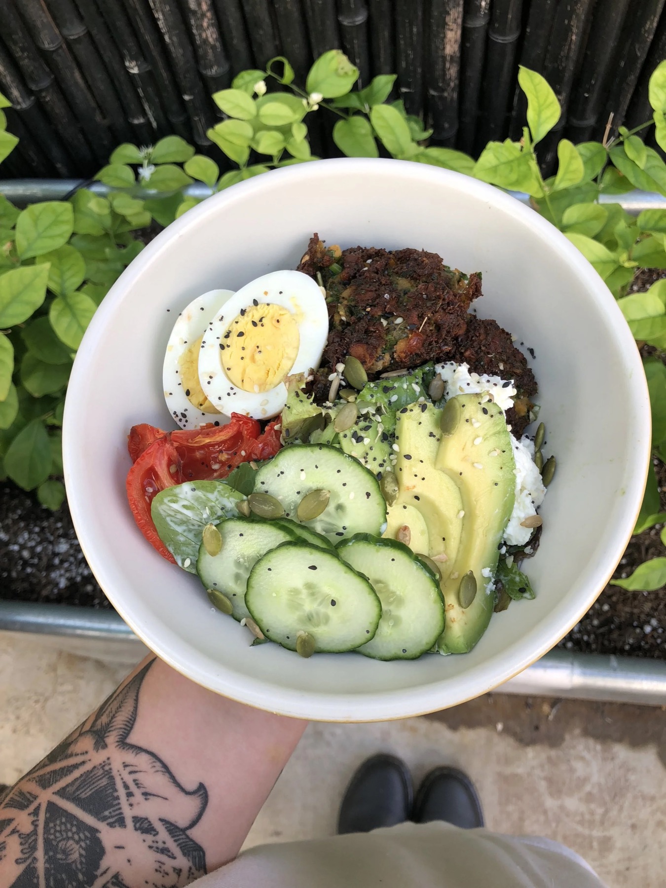 A grain bowl with a boiled egg, avocado, cucumber, tomato and greens
