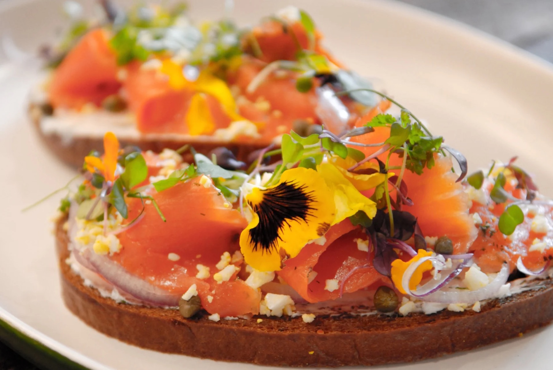 Cured salmon on toasted bread with capers, red onion, microgreens and edible flowers