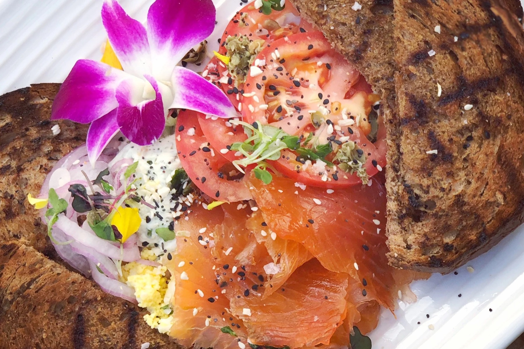 Grilled pumpernickel toast with lox, sliced tomato, red onion and a purple orchid